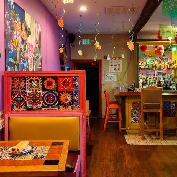 Vibrant Mexican restaurant interior with purple walls, colorful decor, booths, and a fully stocked bar.