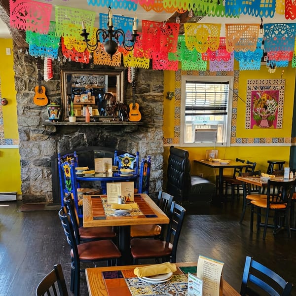 Vibrant Mexican restaurant interior with colorful papel picado, yellow walls, and wooden tables.