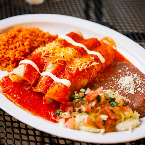 A plate of enchiladas with red sauce, rice, refried beans, and pico de gallo.