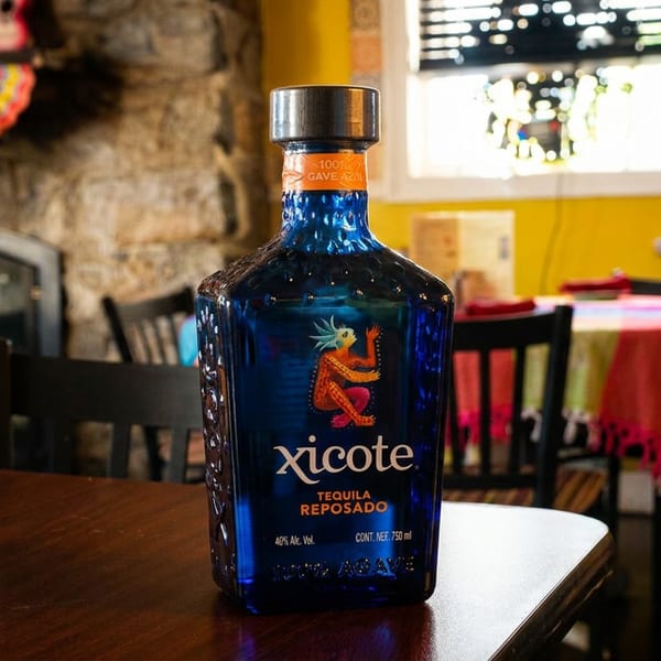 A blue bottle of Xicote Tequila Reposado on a wooden table in a vibrant Mexican restaurant.