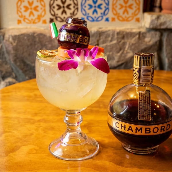 A cocktail with a Chambord miniature bottle and orchid garnish next to a Chambord liquor bottle.