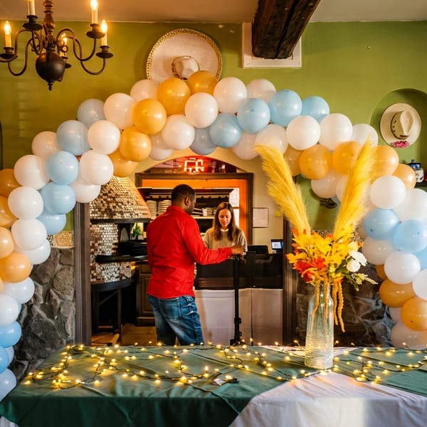 A festive restaurant interior with a balloon arch, string lights, and two people at a counter.
