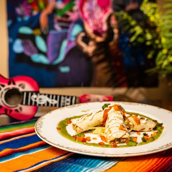 Three enchiladas with green and red sauce on a colorful striped blanket next to a pink toy guitar.